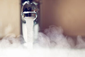 Hot water flowing from a modern faucet with steam rising, representing energy-efficient water heating.